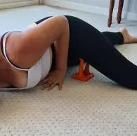 A woman using the Mobilization Magic™ tool under her glute and hip area while lying on an exercise mat. This technique targets glutei and piriformis pain relief through myofascial release.